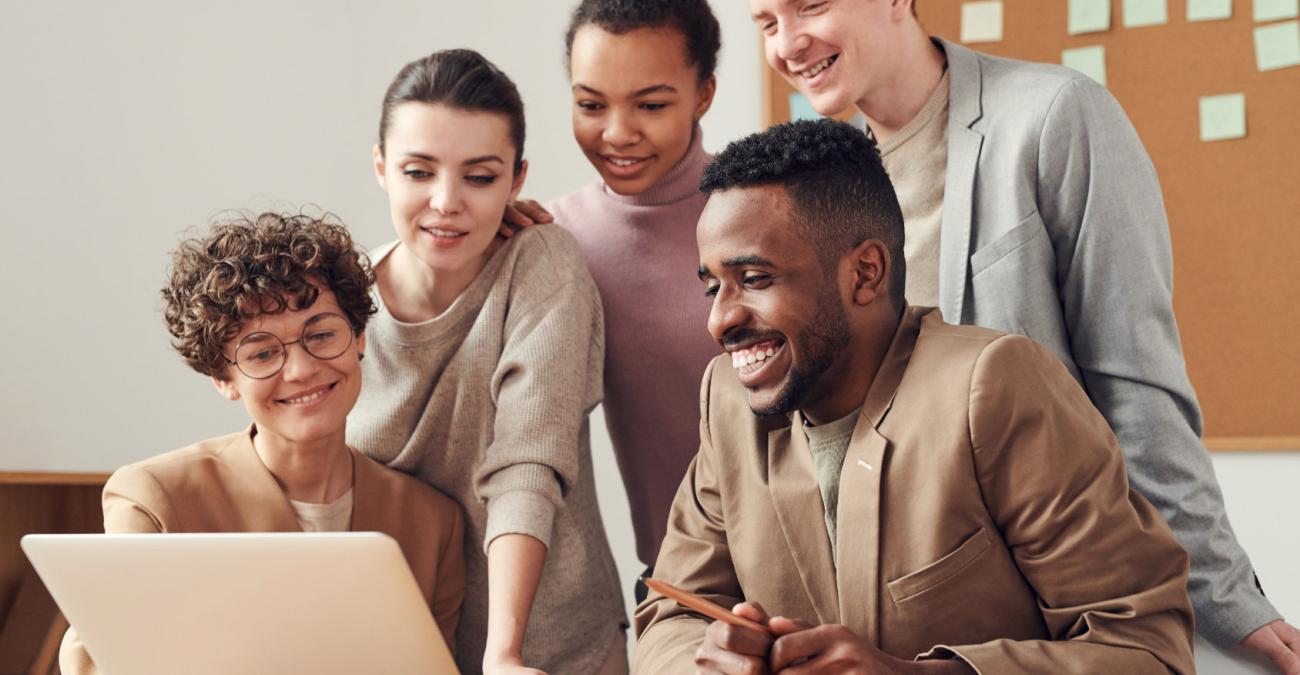 Fünf Menschen sitzen und stehen vor einem Schreibtisch am PC