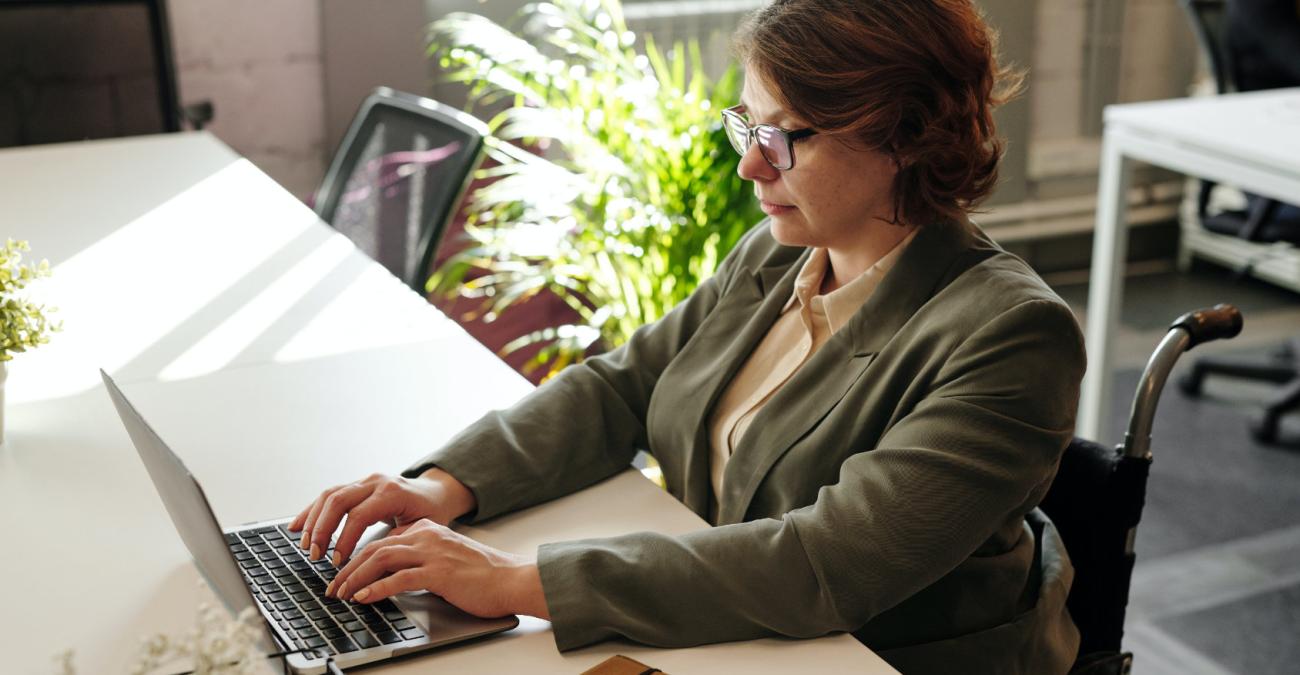 Frau im Rollstuhl sitzt am Schreibtisch vor einem Laptop