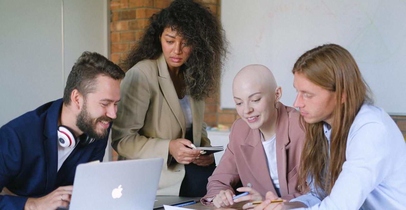 Vier Menschen arbeiten an einem Schreibtisch und schauen in einen PC