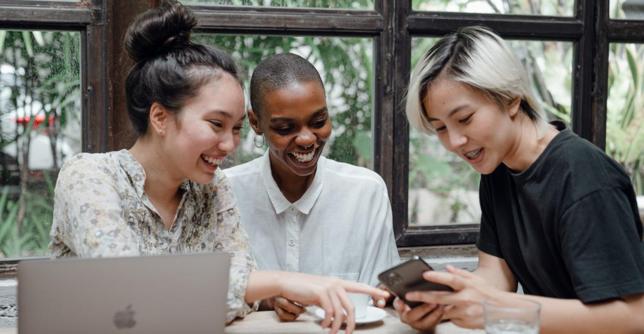 Drei Menschen sitzen am Tisch und schauen auf ein Mobiltelefon