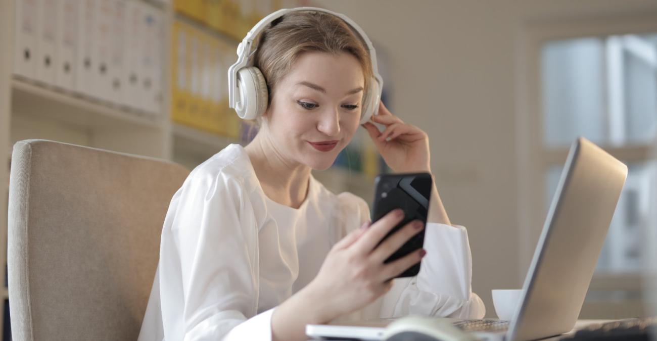 Junge Frau telefoniert mit einem Handy während sie am Laptop sitzt.