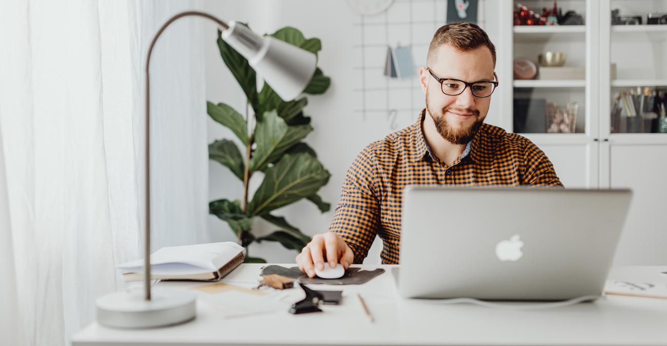 Mensch sitzt am Schreibtisch und arbeitet mit einem Laptop