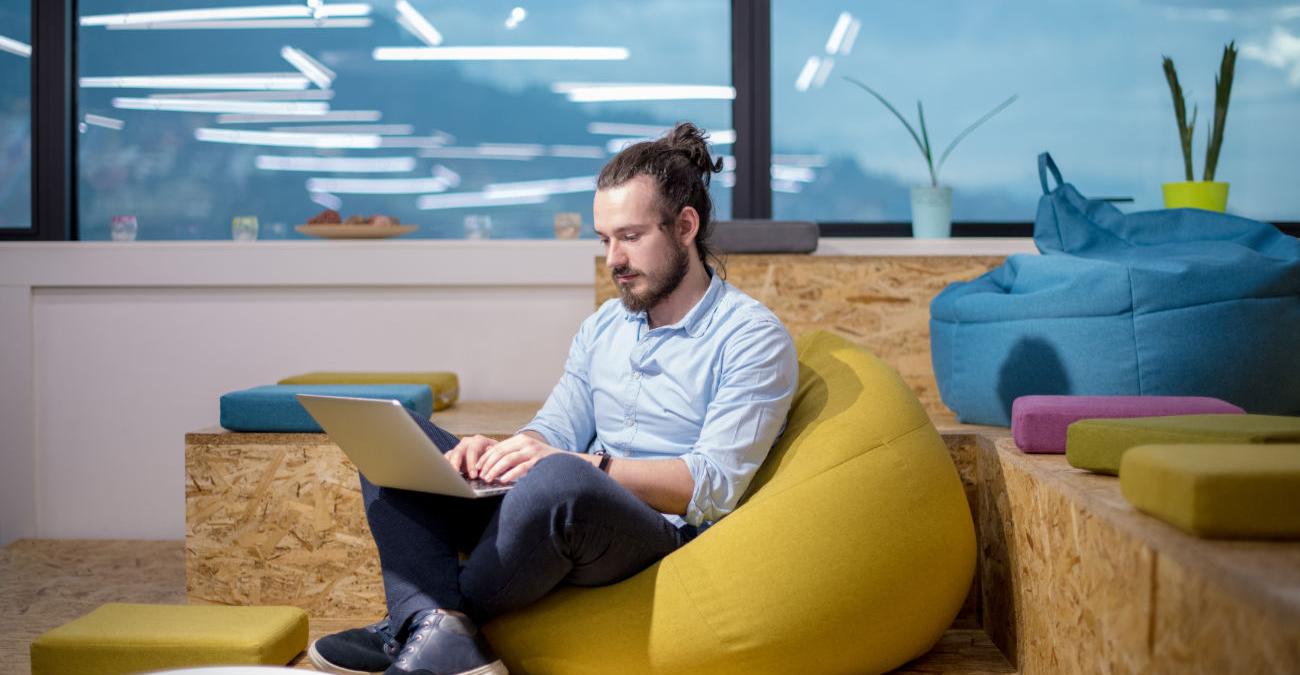 Buntes Wohnzimmer. Junger Mann sitzt mit Notebook auf einem Sitzsack. Er programmiert mit Laravel in Berlin.