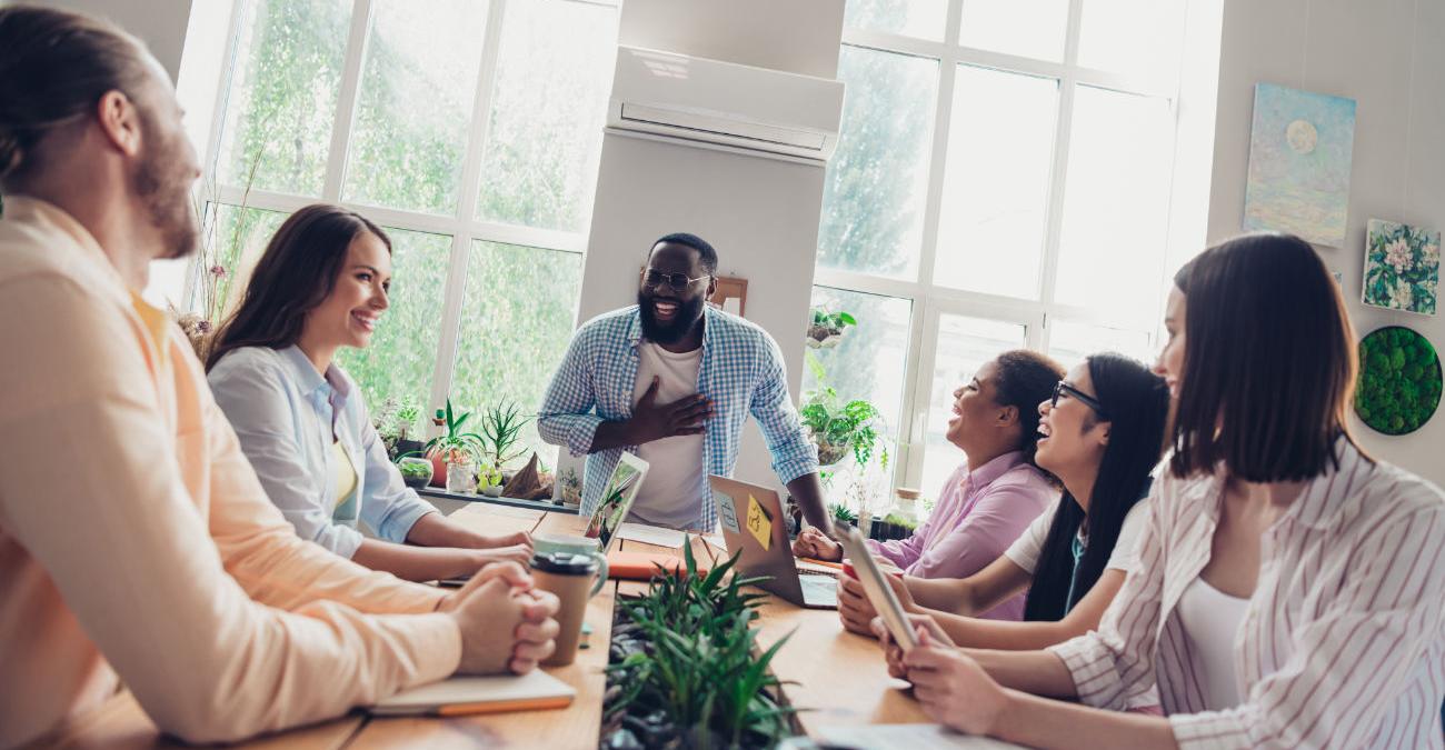 Helles Büro. Frauen und Männer sitzen lachend in einem Meeting. Sie reden über Microsoft .NET.