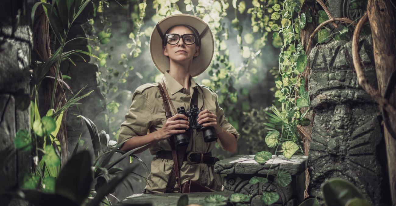 Frau in Tropenkleidung. Sie durchforscht mit einem Fernglas den Dschungel. Ein Sinnbild für den Dschungel aus Daten im Anforderungsmanagement.