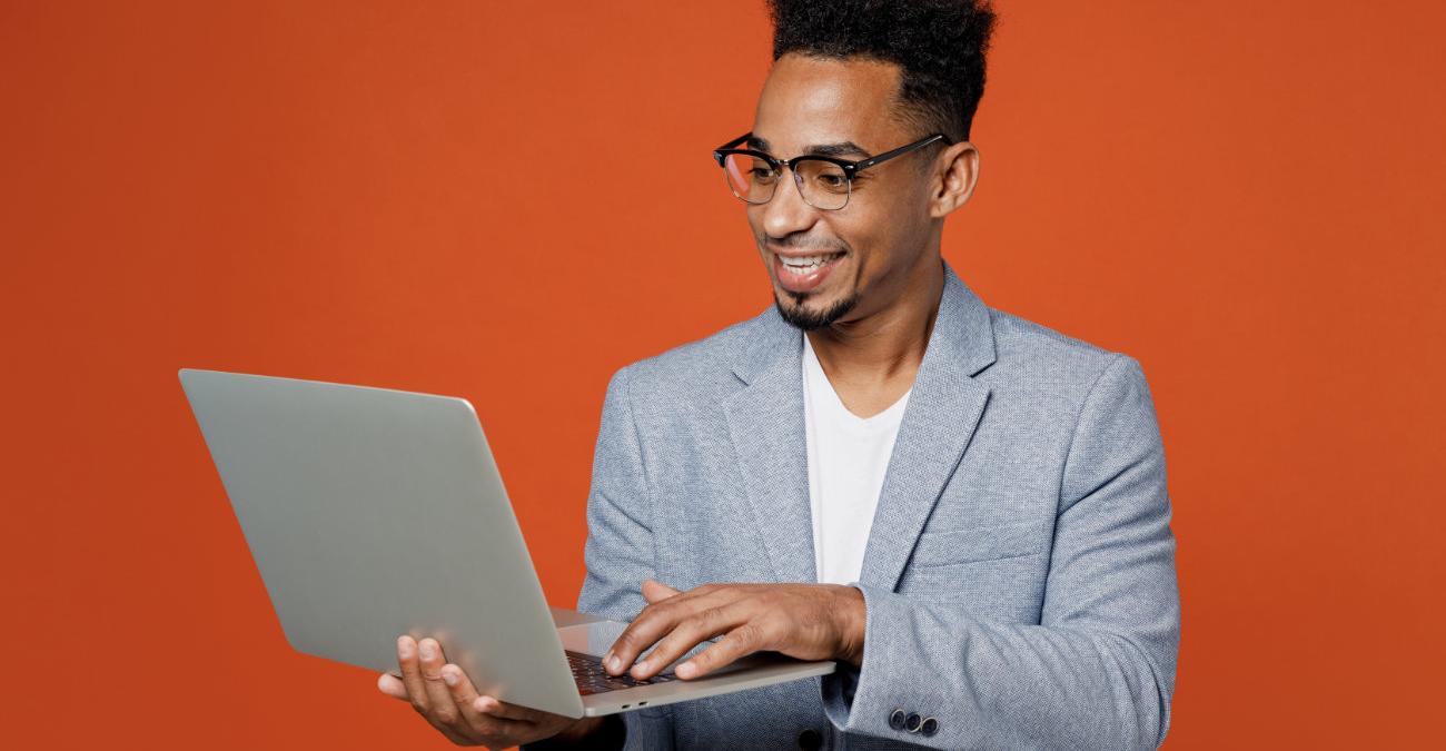 Ein junger, dynamische Mann im Business-Outfit blickt enthusiastisch auf sein Notebook. Er freut sich über die IT-Betreuung.