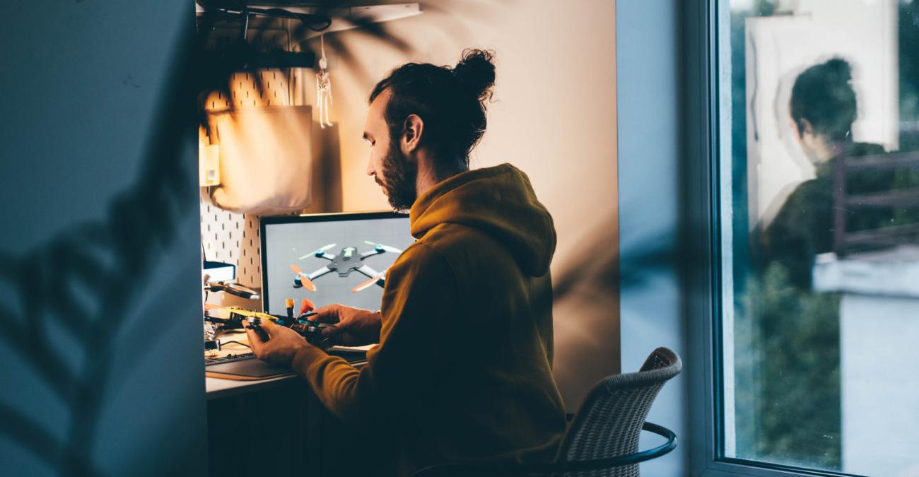 Ein Software-Dienstleister sitzt an seinem Laptop. Er arbeitet an einer Drohne, deren Software gewartet werden muss.