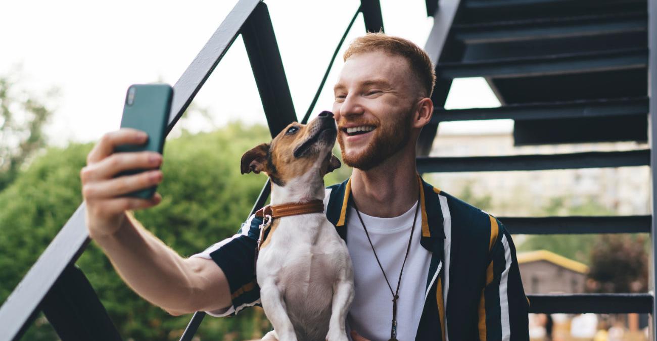 Junger Mann macht ein Selfie mit seinem Hund. Er will es mit dem Messenger verschicken.