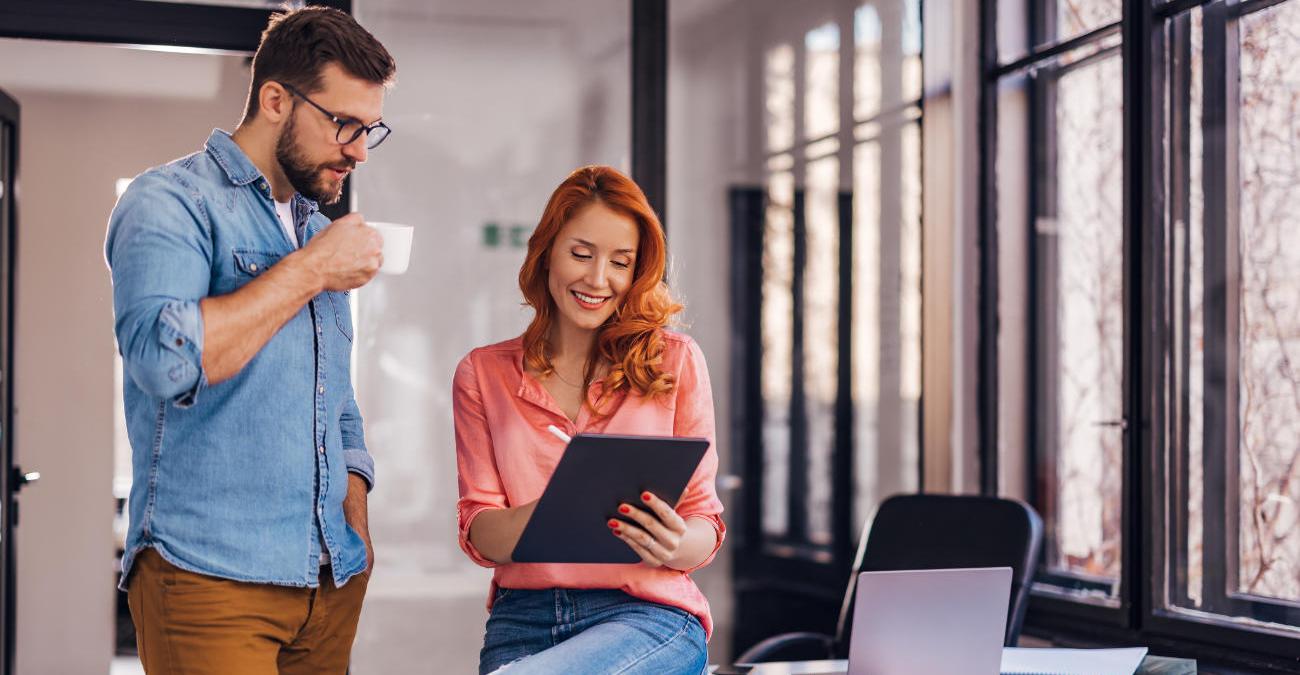 Ein Mann und eine Frau im Büro. Sie blicken gemeinsam auf ein Tablet. Sie sind App-Entwickler bei der Arbeit.