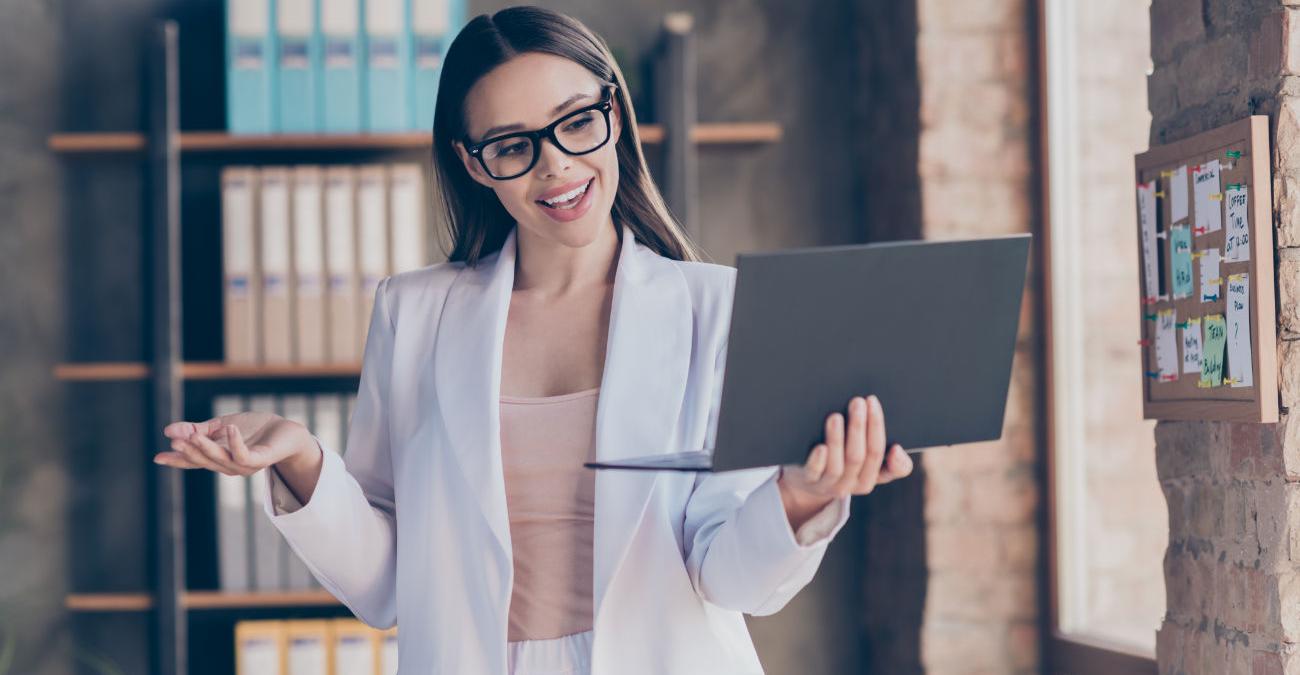 Ein schöne und intelligente junge Frau steht im Office. Sie hält lächelnd ein Notebook in der Hand und freut sich über die Ergebnisse der Business Intelligence.