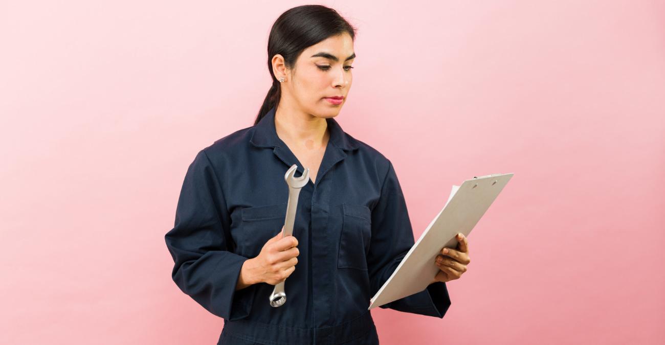 Eine junge Frau im Mechaniker-Dress betreibt Konfigurationsmanagement. Sie hält einen Schraubenschlüssel und blickt auf ein Klemmboard