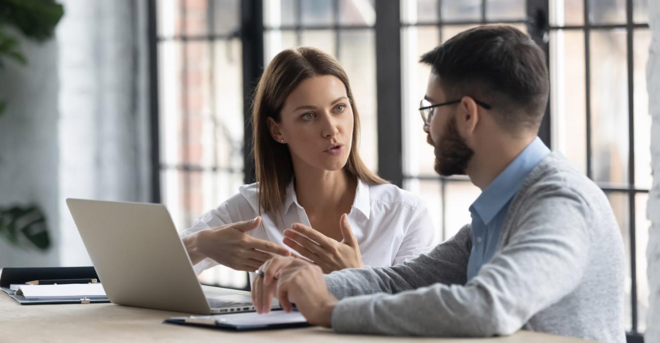 Eine Kollegin erklärt im Büro ihrem Kollegen den Begriff IT-Compliance.