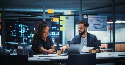 Ein Mann und eine Frau sitzen im Büro vor ihren Notebooks. Sie unterhalten sich angeregt über die neue Firmensoftware.