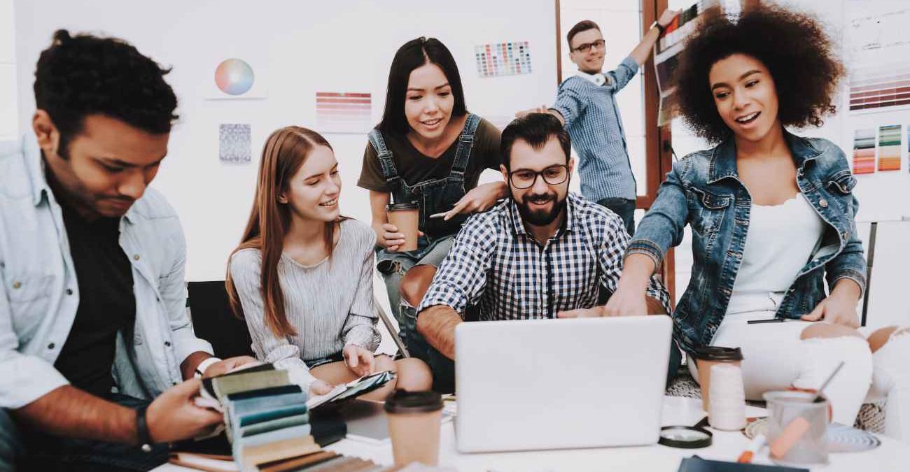 Junge dynamische Mitarbeiter:innen blicken auf ein Notebook im Büro. Sie bestaunen die neue Projektmanagement-Software.