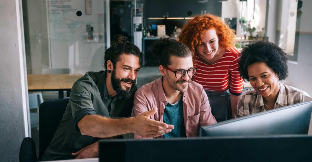 Ein dynamische Team in einem IT-Unternehmen. Männer und Frauen. Sie blicken enthusiastisch auf einen Monitor.