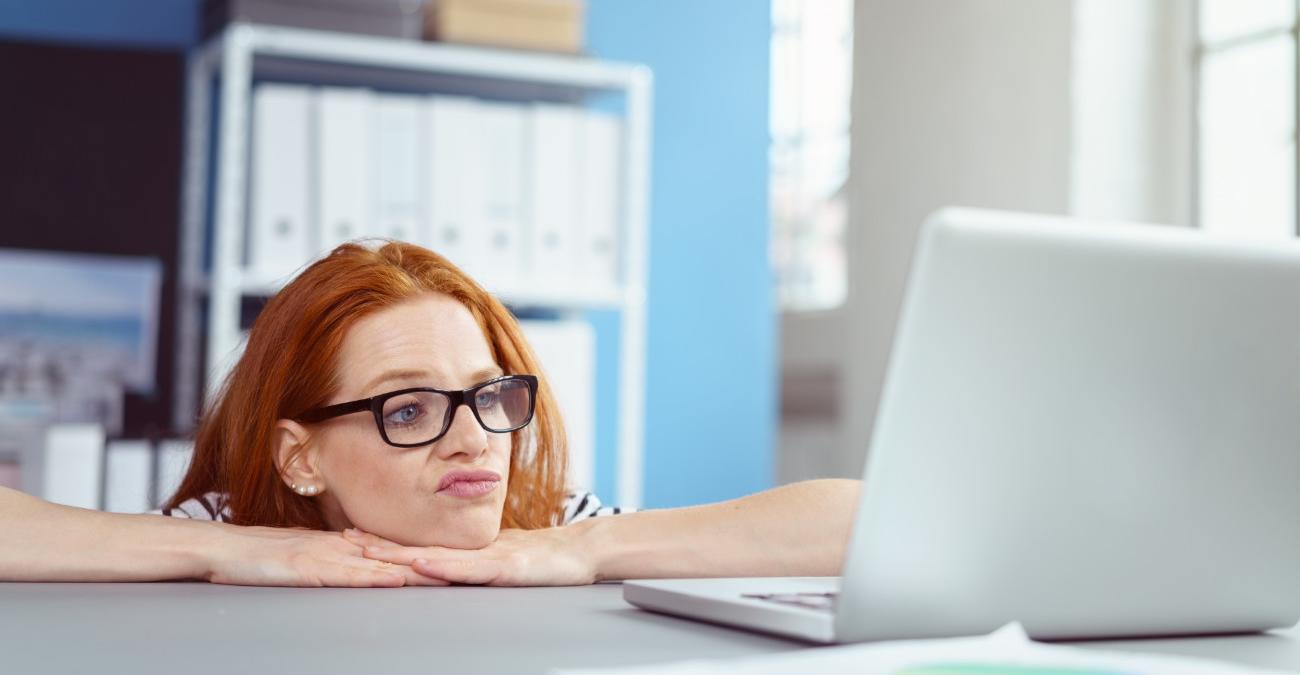 Im Büro: Ein junge Frau hat ihren Kopf auf die Hände gestützt. Sie blickt verwirrt auf ihr Notebook, auf dem ein neues Outlook installiert ist.