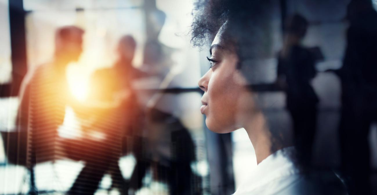 Eine Frau im Business-Dress. Sie blickt aus dem Büro durch eine Fensterscheibe auf die Zukunft: Die KI-Trends 2025.