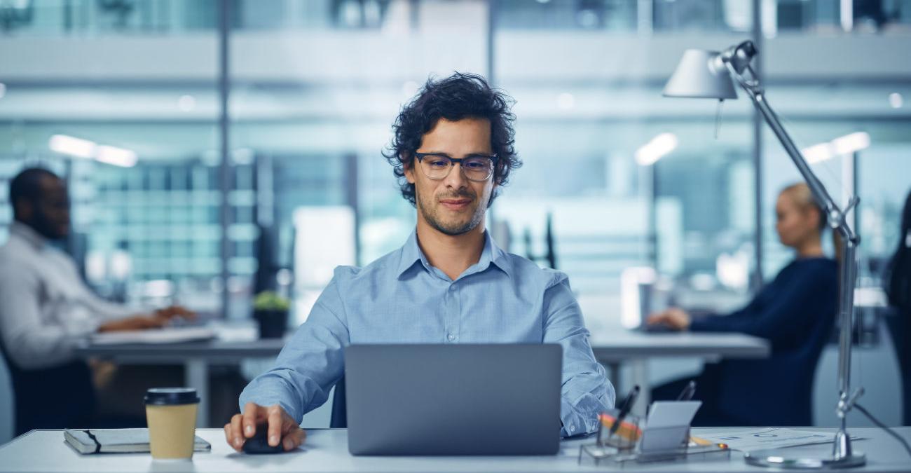 Ein dynamischer junger Unternehmer sitzt vor seinem Notebook im Büro. Er testet die neue Unternehmer-Software.