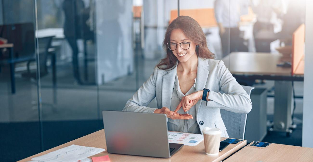 Barrierefreie Software Eine junge Frau im Businessdress sitzt im Büro vor ihrem Notebook. Sie führt eine Videokonferenz in Gebärdensprache. Dazu nutzt sie barrierefreie Software.