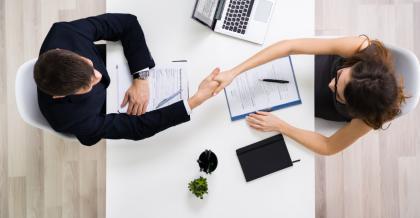 Vogelperspektive: Ein Mann und eine Frau sitzen sich beim Bewerbungsgespräch gegenüber und schüttel sich die Hand. Das symbolisiert erfolgreiches Digitales Recruiting mit KI.
