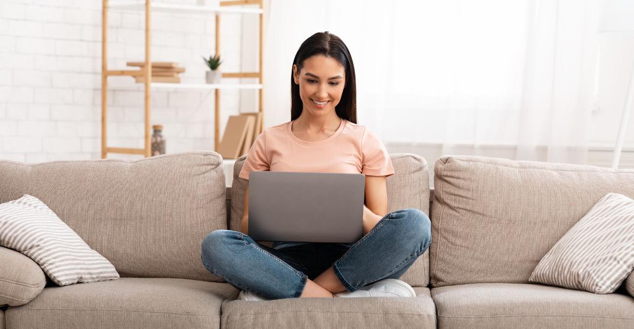 Eine junge Frau sitzt auf dem Sofa beim Online-Shopping. Sie profitiert vom Magento E-Commerce.