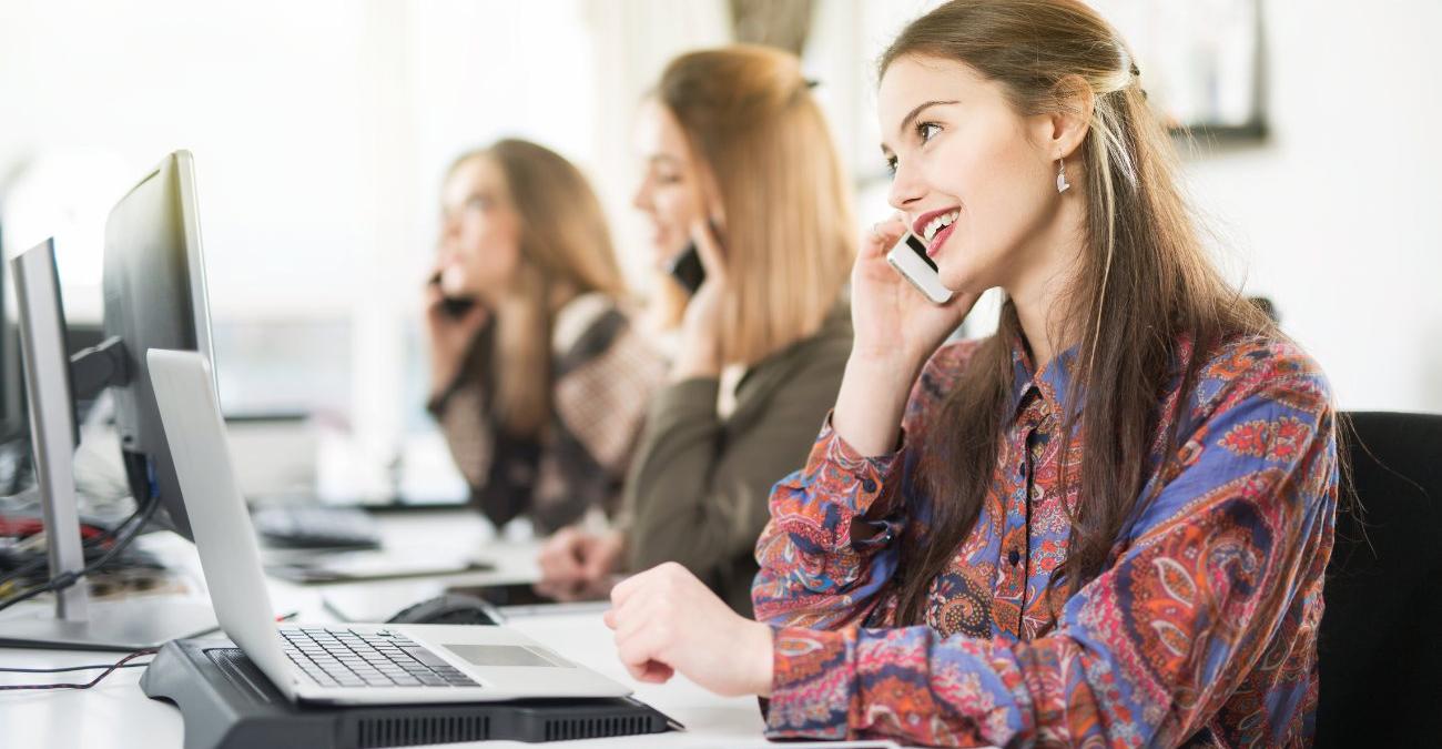 Ein nette IT-Mitarbeiterin sitzt zusammen mit anderem im Büro vor ihrem Notebook. Sie bietet einem Kunden IT-Infrastruktur-Services an.