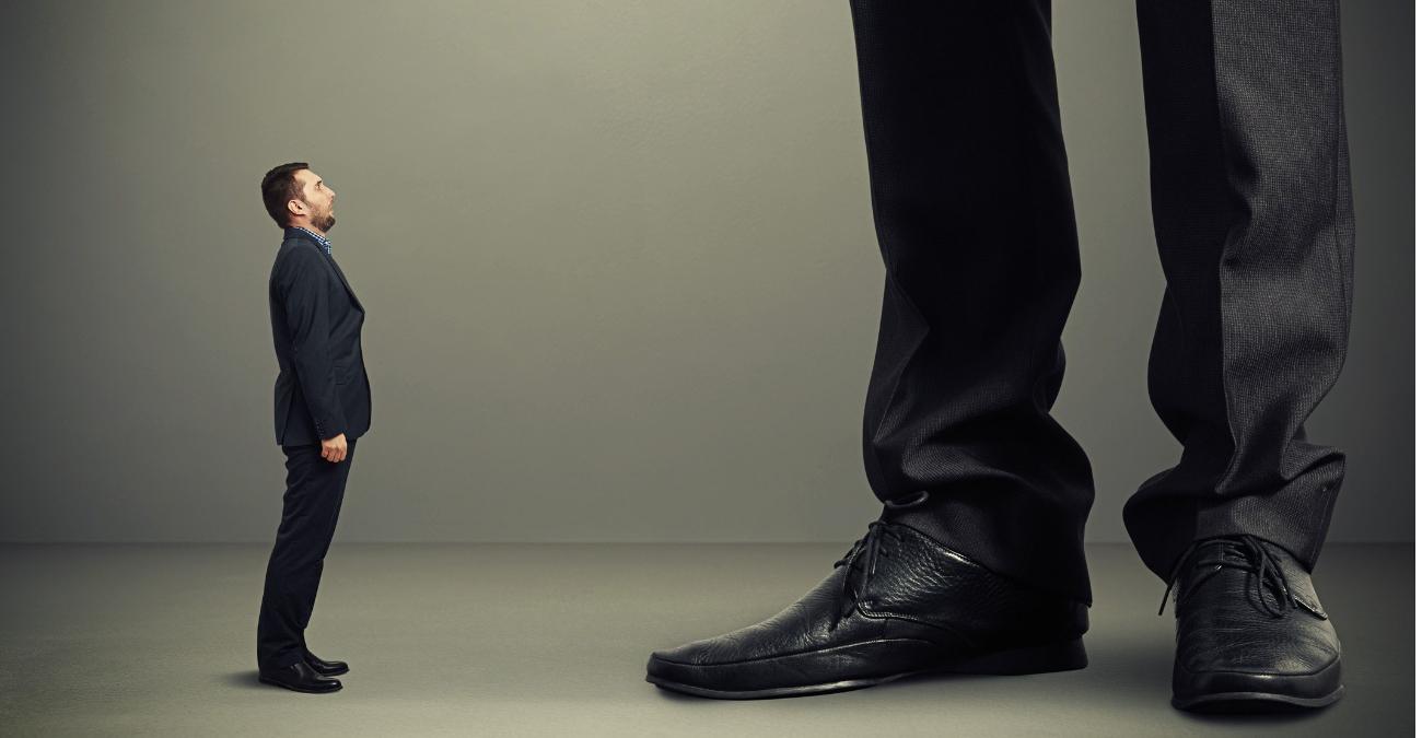 Ein kleiner Mann im Business Outfit blickt an an den Beinen eines riesigen Mannes empor. Ein Symbolbild für die Datensouveränität im Konzern.
