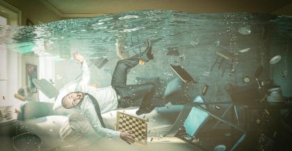 Ein Wohnzimmer steht völlig unter Wasser. Zwischen im Wasser schwebenden Möbeln treibt überrascht ein Mann. Ein eugenzwinkerndes Bild, das zeigt, dass krisenmanagement-software Hilfe für jederman sein kann.