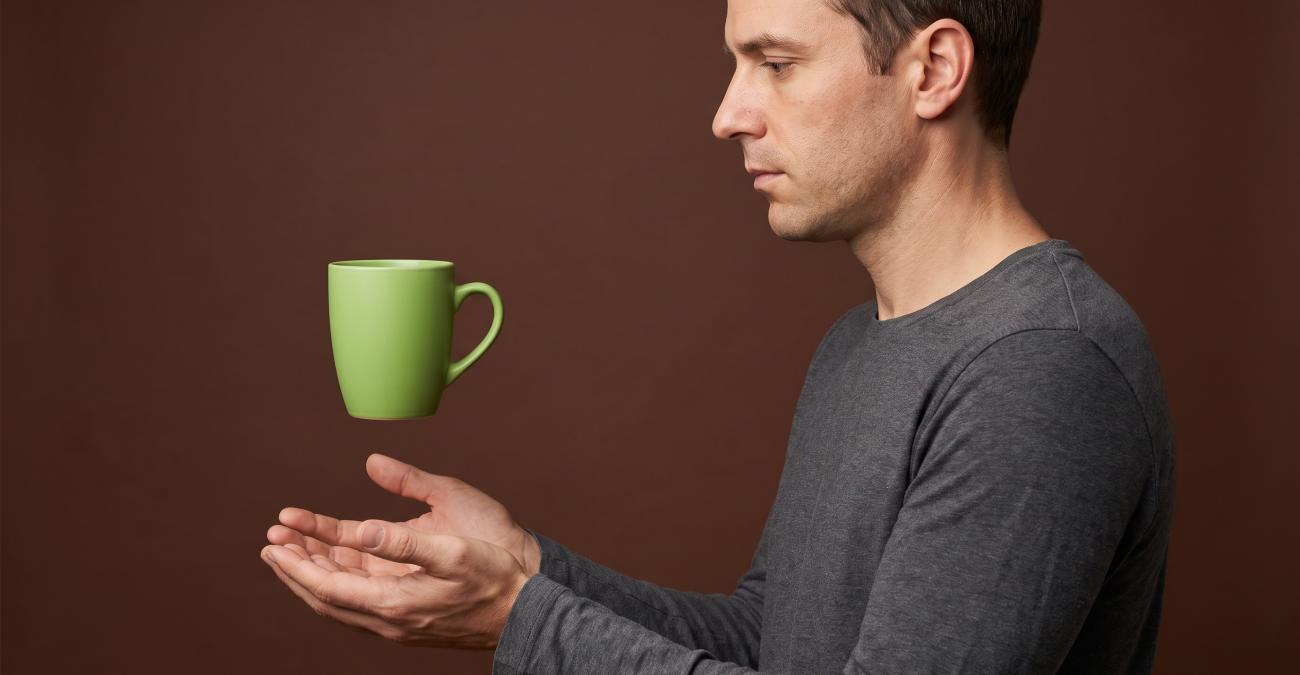 Ein Mann hält beide Hände fangbereit unter eine Tasse, die noch reglos in der Luft steht. Sinnbild für einen Wartungsvertrag, der die Reaktion vorab verbindlich festlegt.