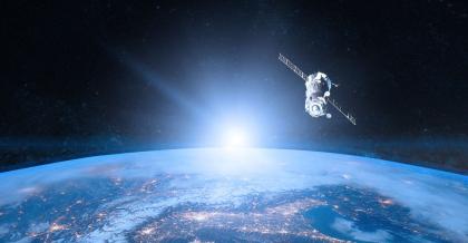 Die Erde vom Weltall betrachtet. Die Sonnenstrahlen bahnen sich ihren Weg daran vorbei. Ein Satellit für Erdbeobachtung schwebt darüber.