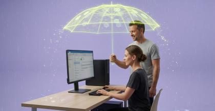 Eine Frau arbeitet an einem Schreibtisch mit Rechner und Monitor, hinter ihr hält ein Kollege einen leuchtend gelbgrünen, digitalen Schirm aus Lichtlinien über den ganzen Arbeitsplatz, während ringsum Regen fällt. Sinnbild dafür, dass Hersteller mit der neuen Produkthaftung Verantwortung für die Sicherheit ihrer Software übernehmen.