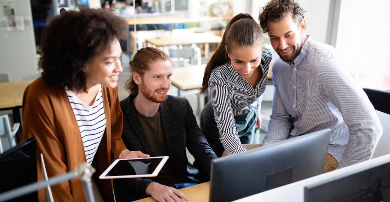 Das Team einer Softwareagentur schaut gemeinsam auf einen Bildschirm und entwickelt Software für KMU im Kundenauftrag.