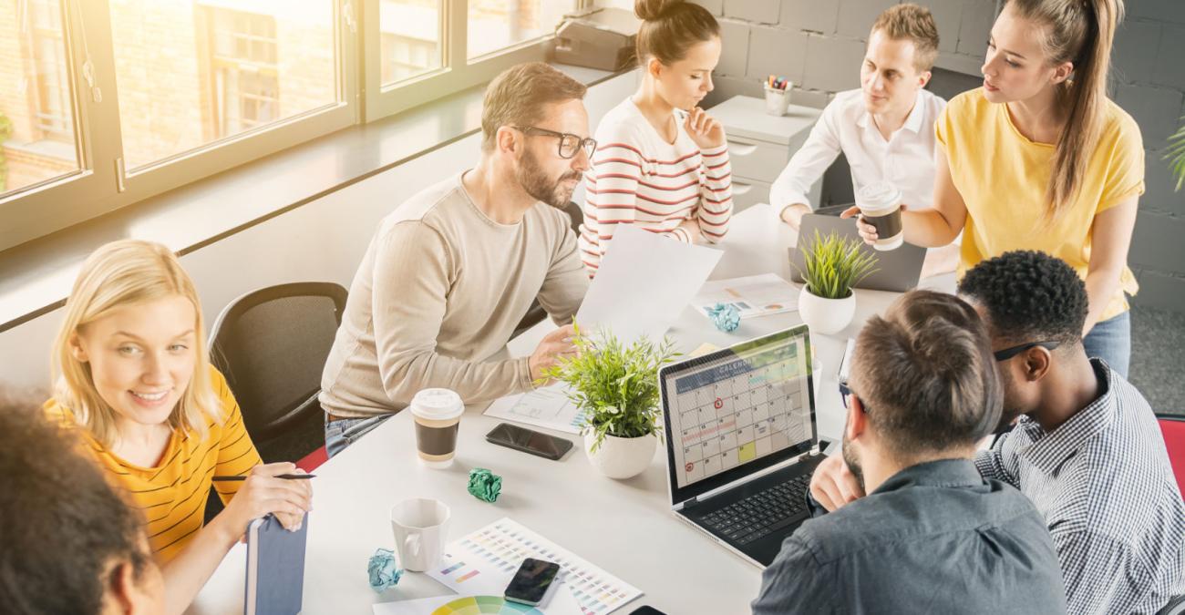 Mitarbeiter*innen einer Webagentur in Berlin sitzen an einem Tisch und planen ihr Vorgehen an Laptops und handschriftlichen Notizen.